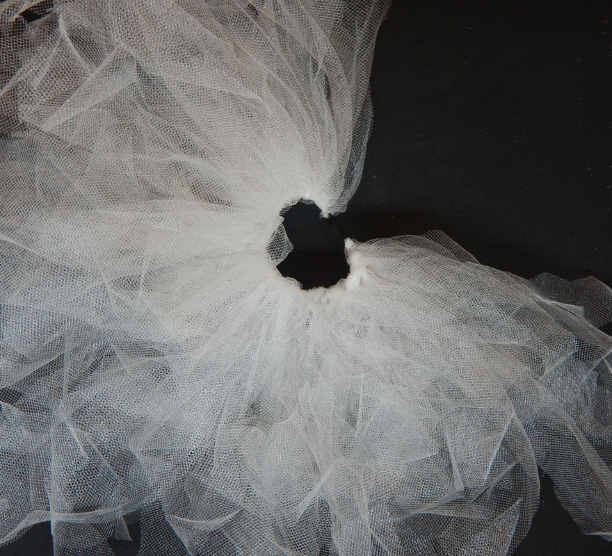 Multiple pieces of white tulle are attached to a black elastic band. The band is covered about seventy five percent. 