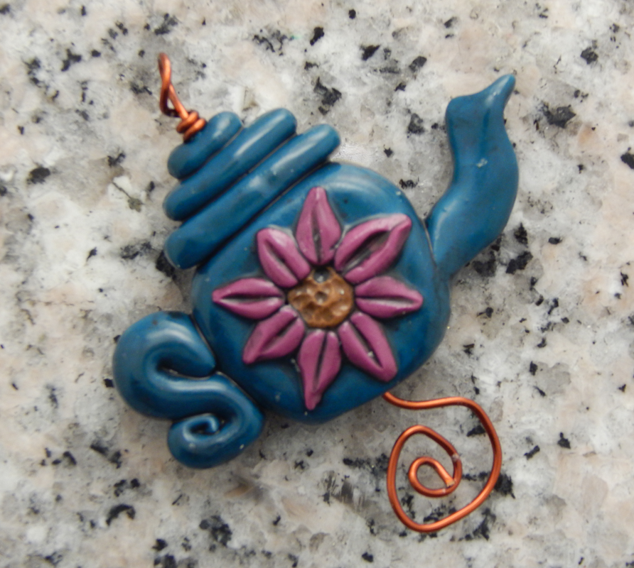 A blue teapot bad with a pink flower on a wire