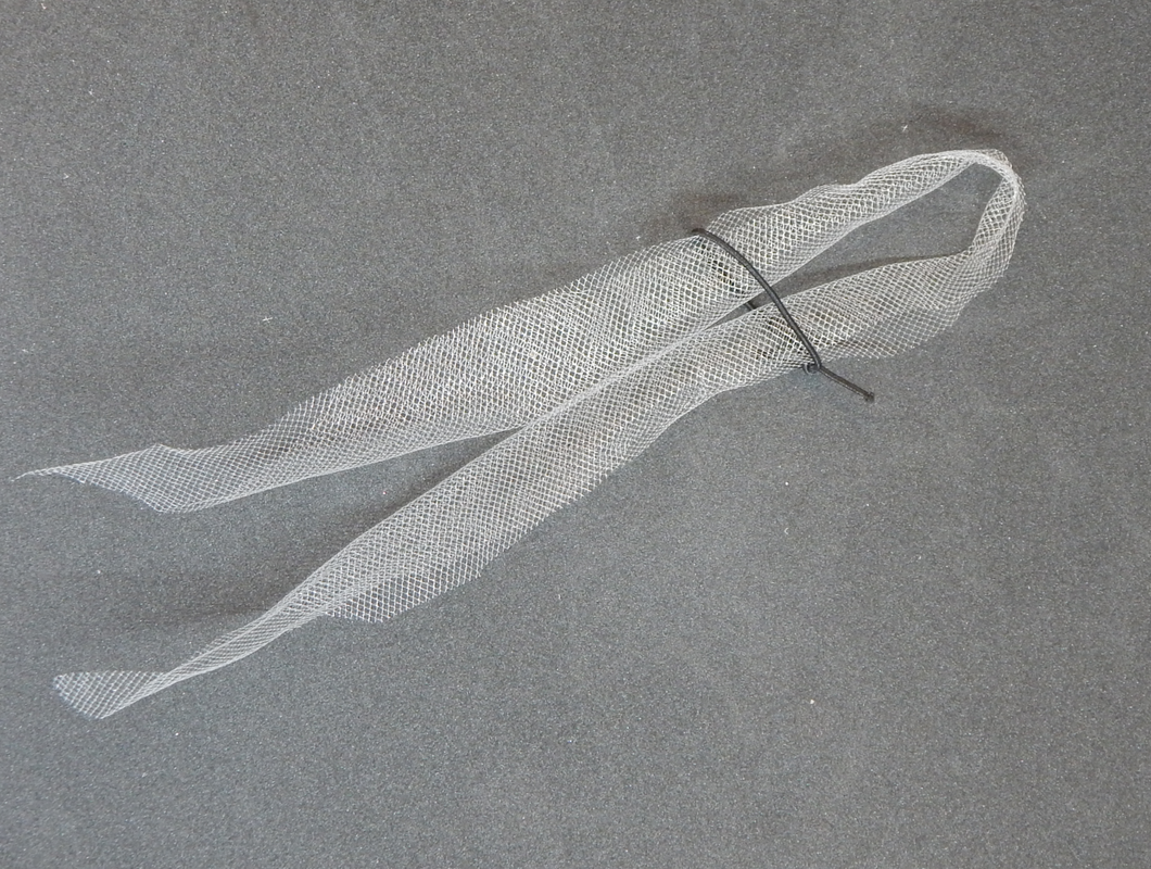 A piece of white tulle is folded in half with a black elastic band encircling it a fe inches down.