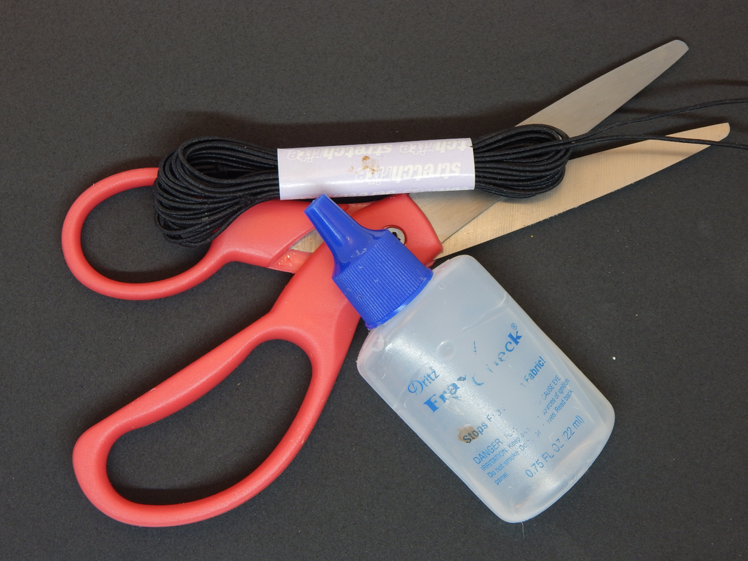 A picture of pink handled scissors, with a bottle of fray check and a bundle of black elastic cord on top on a black background